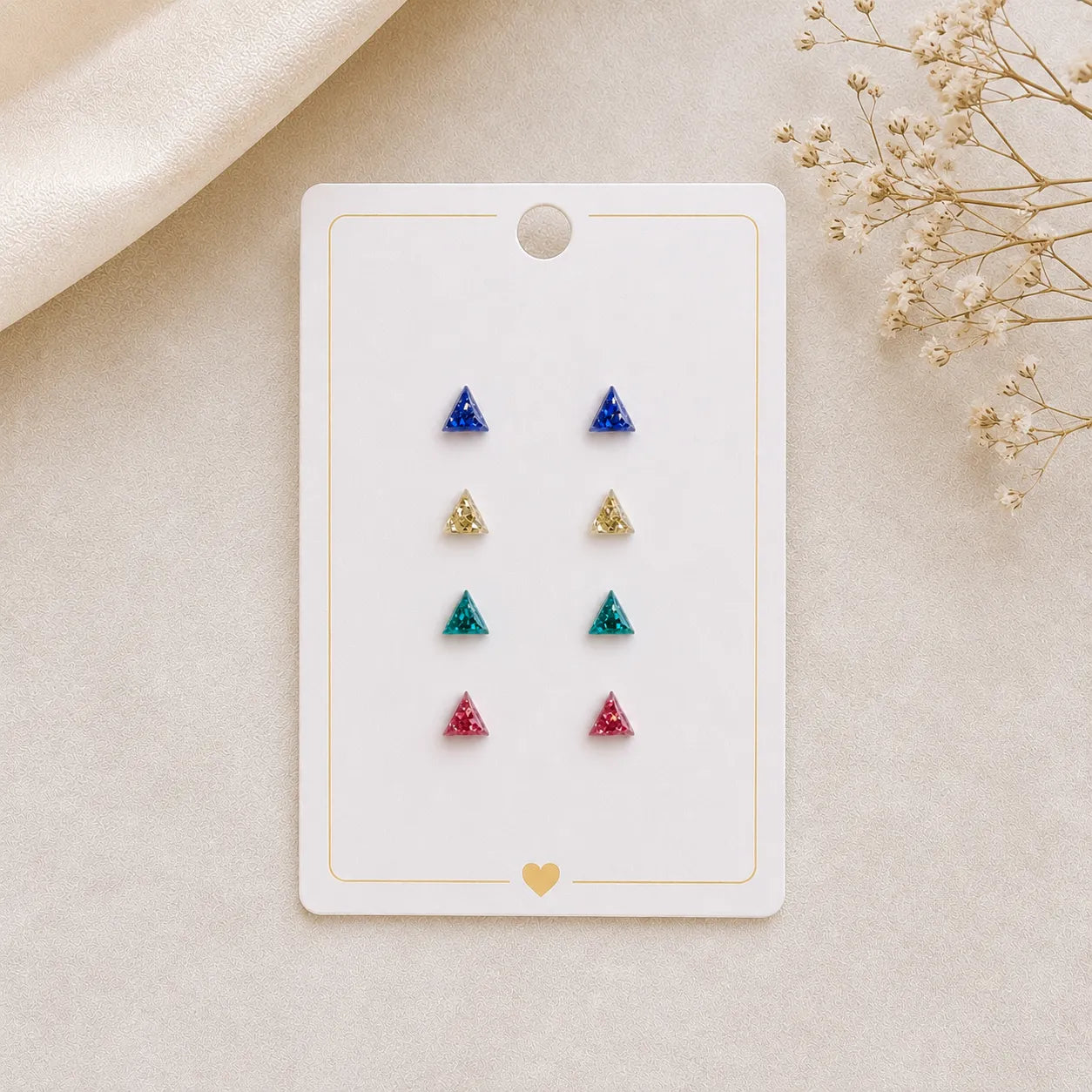 Set of triangle-shaped earrings on a display card with dried flowers on a beige background