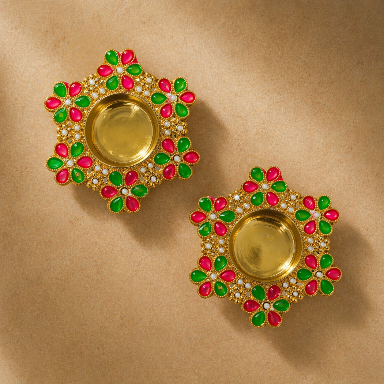 Pair of gold earrings with green and pink gemstones on a beige background