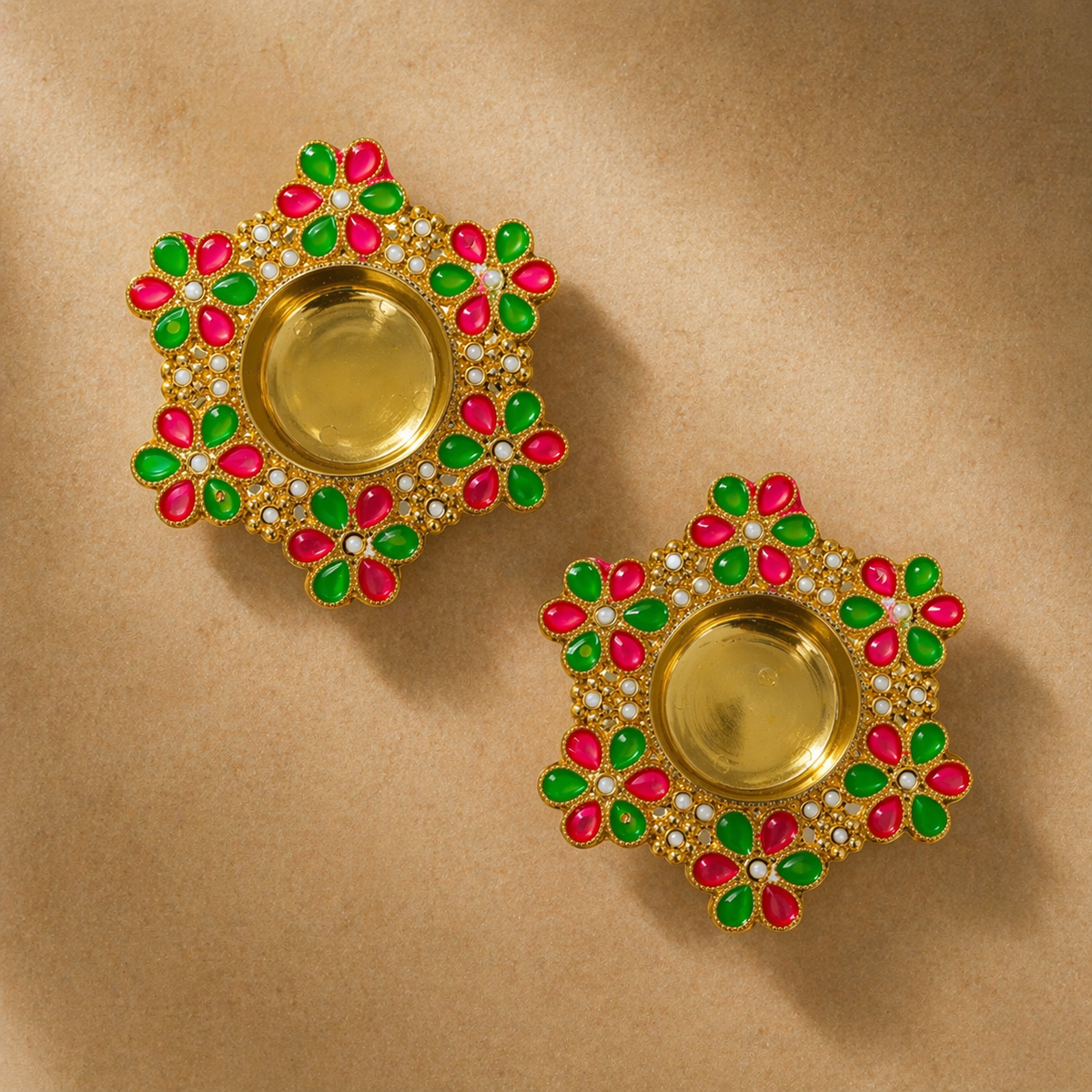 Pair of gold earrings with green and pink gemstones on a beige background