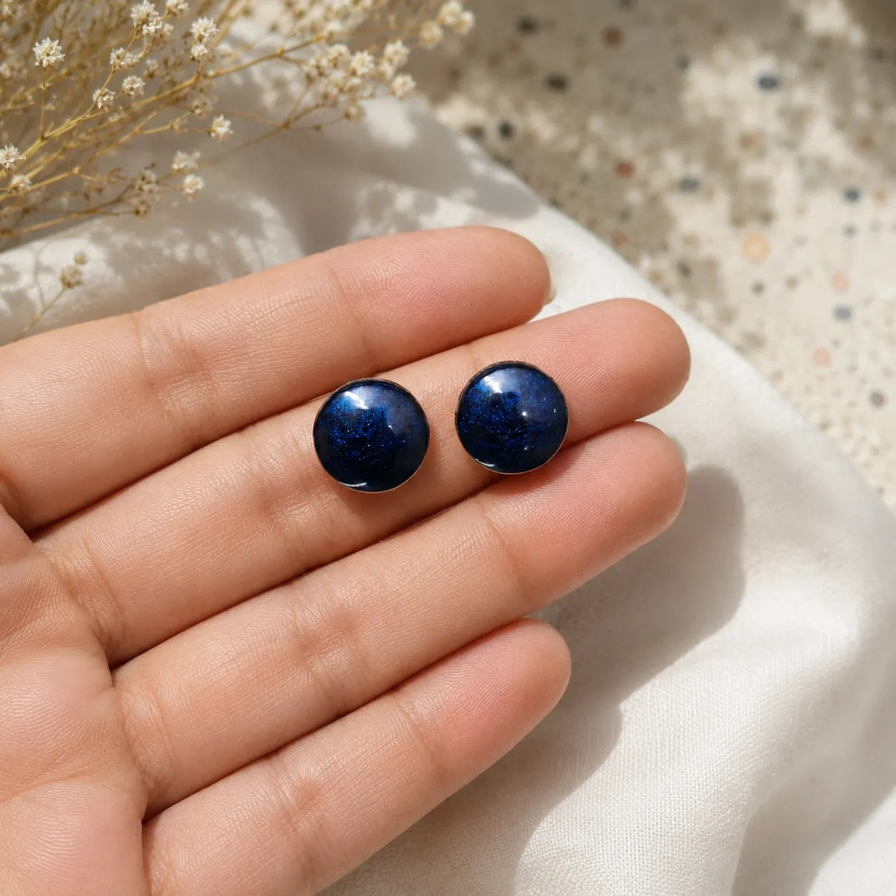 Handmade navy blue glossy resin stud earrings with metallic shimmer finish held in hand under soft natural lighting.