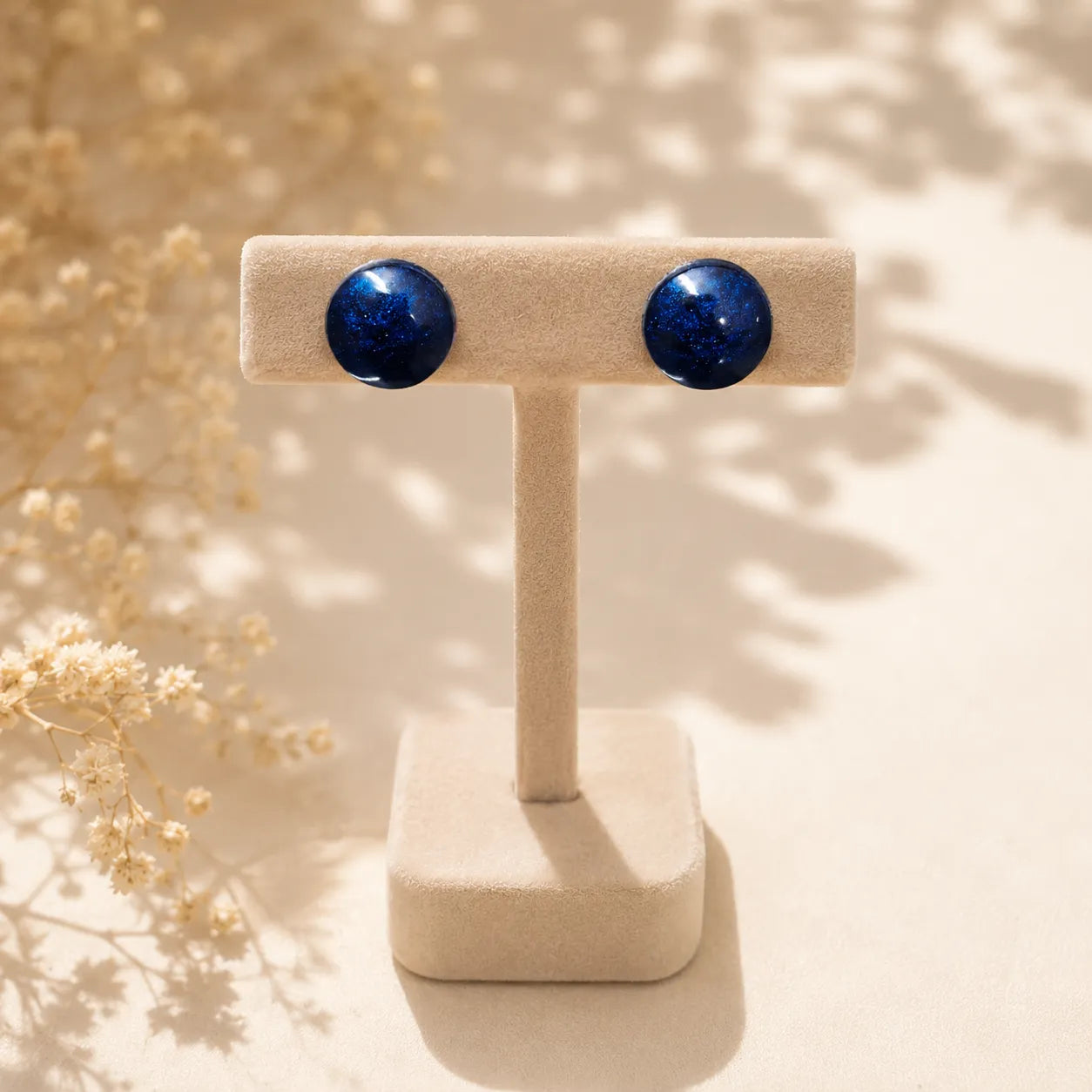 Handmade navy blue glossy resin stud earrings displayed on a beige velvet jewellery stand with metallic shimmer finish and premium minimal styling
