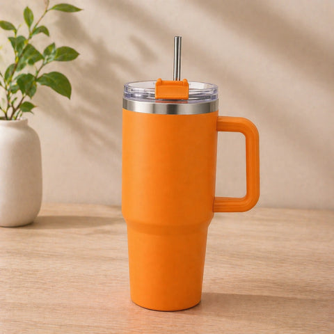 Orange insulated mug with handle and straw on a wooden surface with a beige background