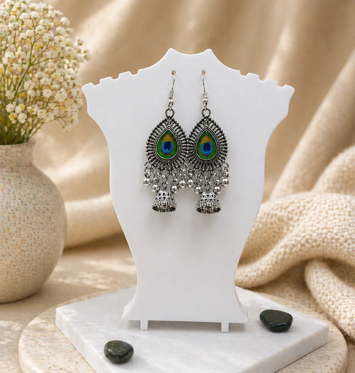 Pair of peacock feather earrings on a white stand with a neutral background
