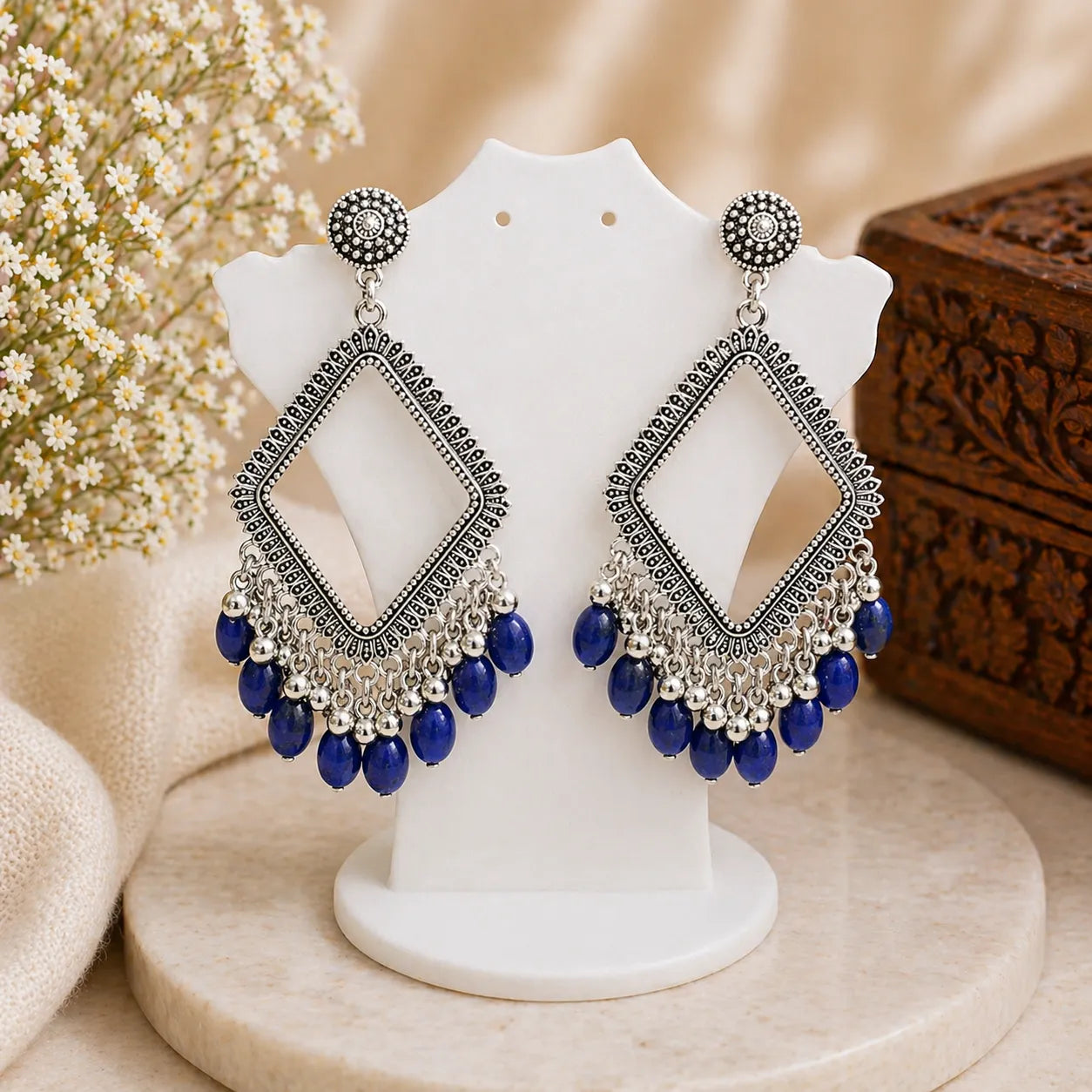 Ornate earrings with blue beads on a white stand against a neutral background