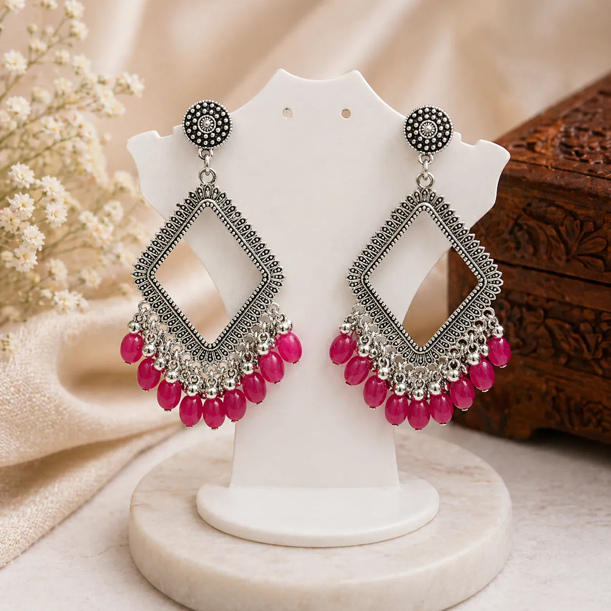 Ornate silver earrings with pink beads on a white stand against a neutral background
