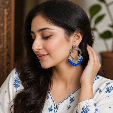 Woman wearing a pair of large, decorative earrings with blue beads.
