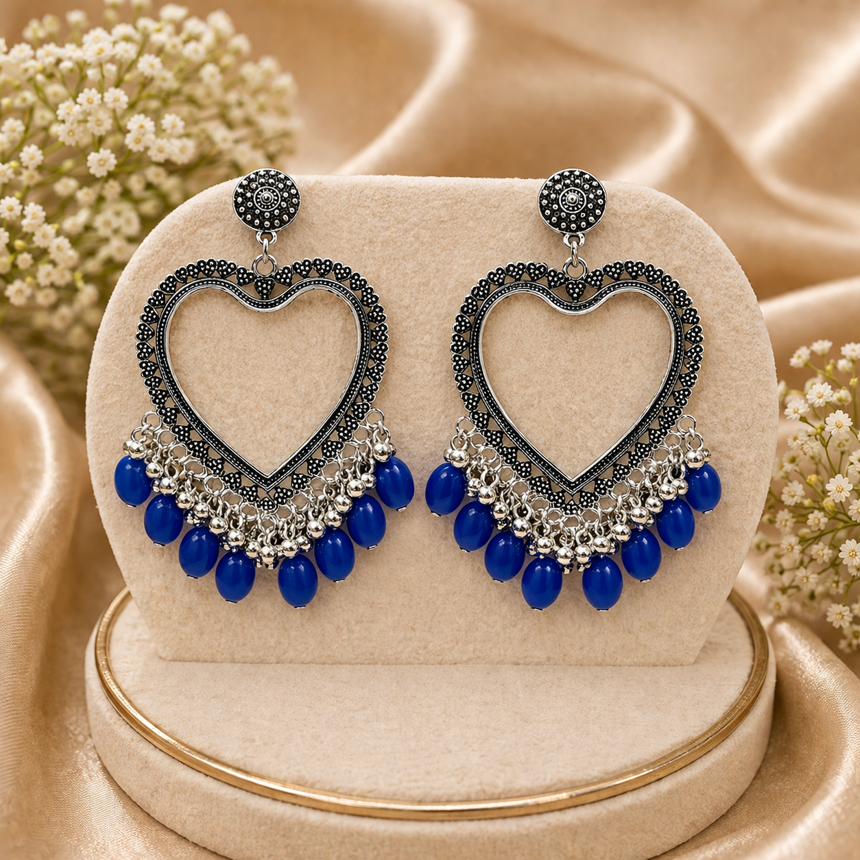 Heart-shaped earrings with blue beads on a beige stand with flowers in the background