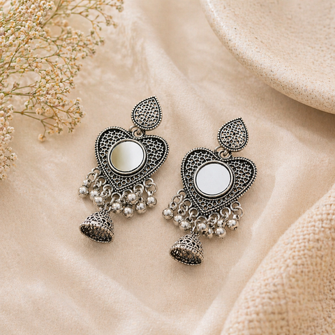 Ornate silver earrings with heart-shaped central stones on a beige fabric background