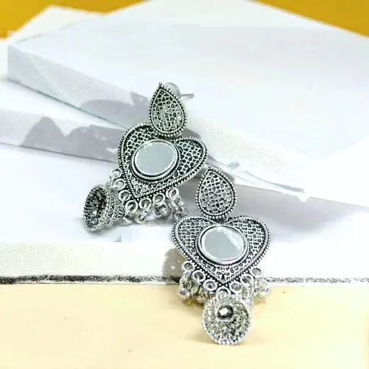 Silver earrings with intricate designs on a white fabric background