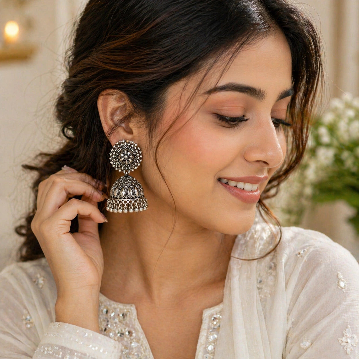 Woman wearing silver jhumka earrings, smiling, with a blurred background