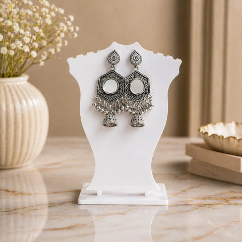 Pair of silver earrings on a white stand with a decorative background