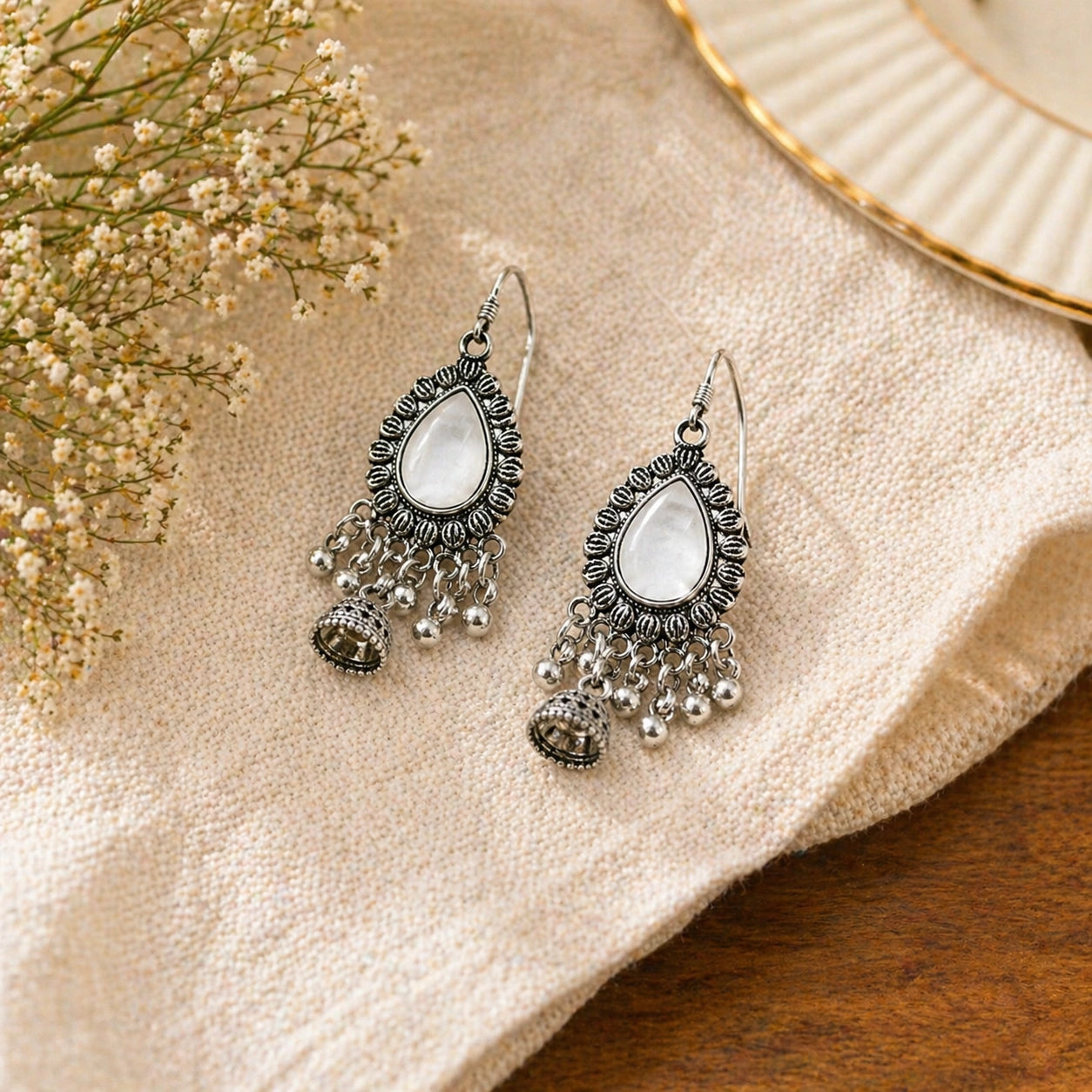 Oxidised silver mirror drop jhumka earrings with teardrop design and hanging beads placed on fabric background