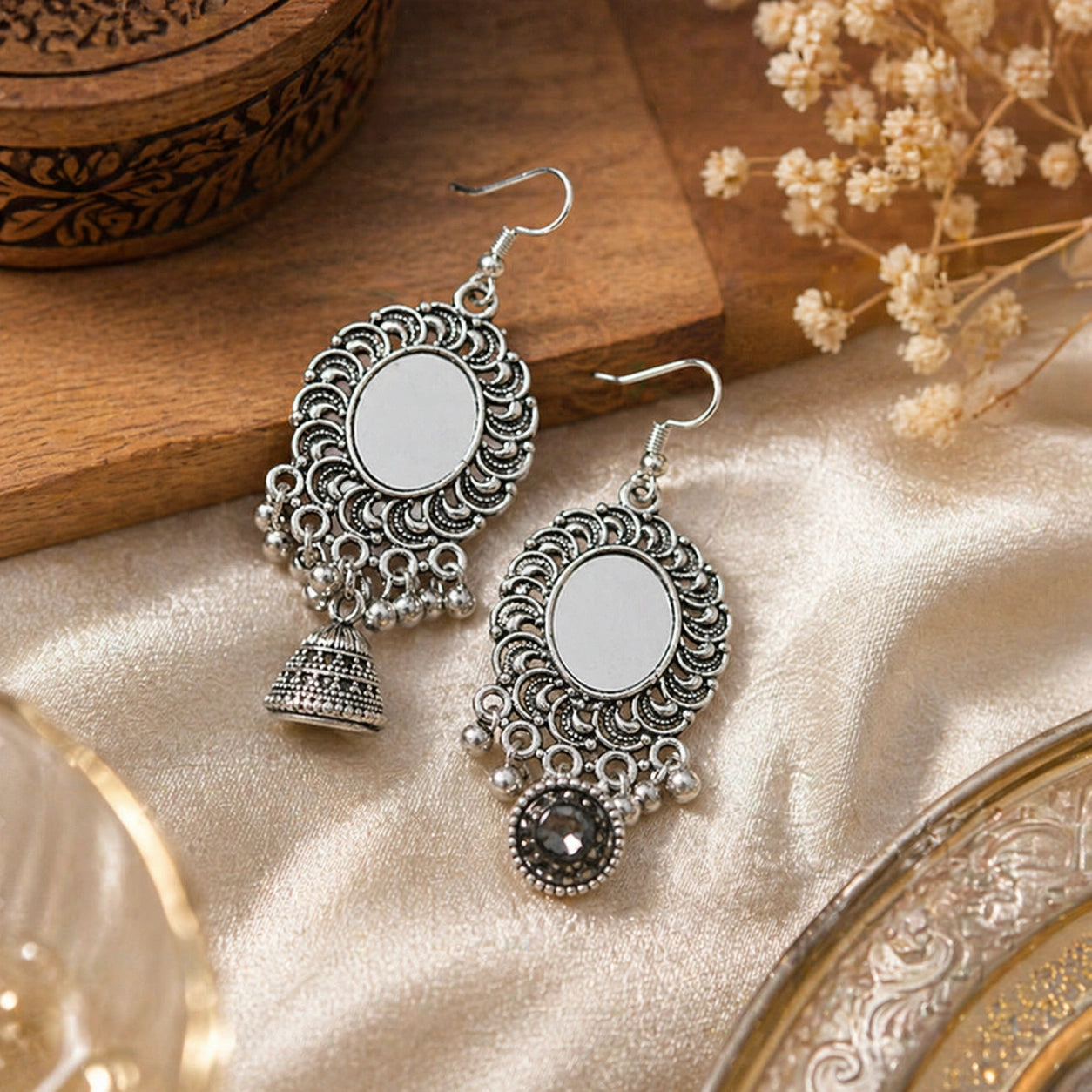 Pair of silver earrings on a textured surface with decorative elements.
