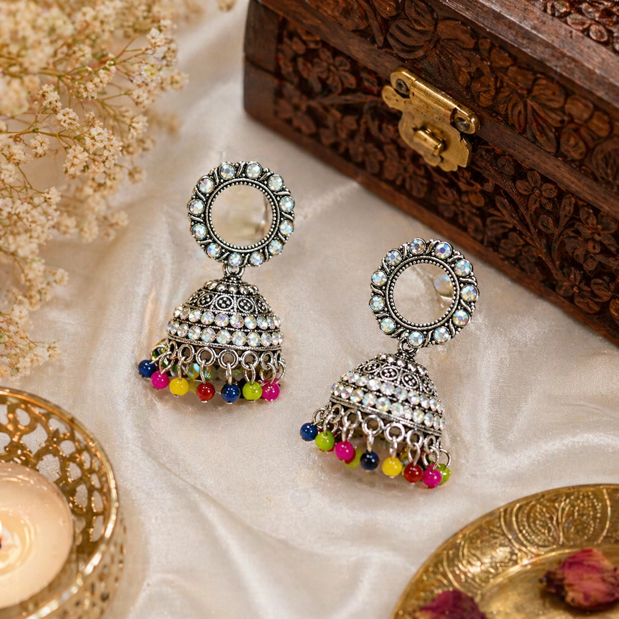 Decorative earrings with colorful beads on a textured surface with a wooden box in the background.
