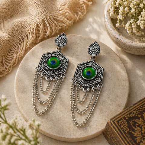 Ornate silver earrings with green gemstones on a stone surface with natural elements.