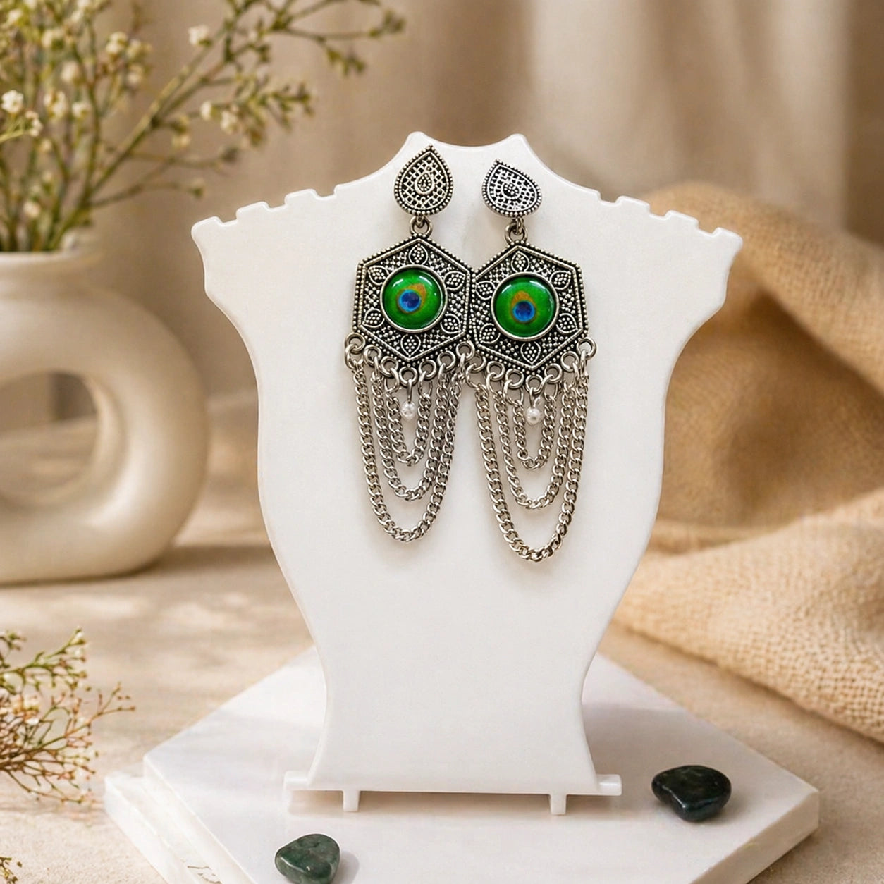 Pair of earrings with green eyes on a white stand with a neutral background