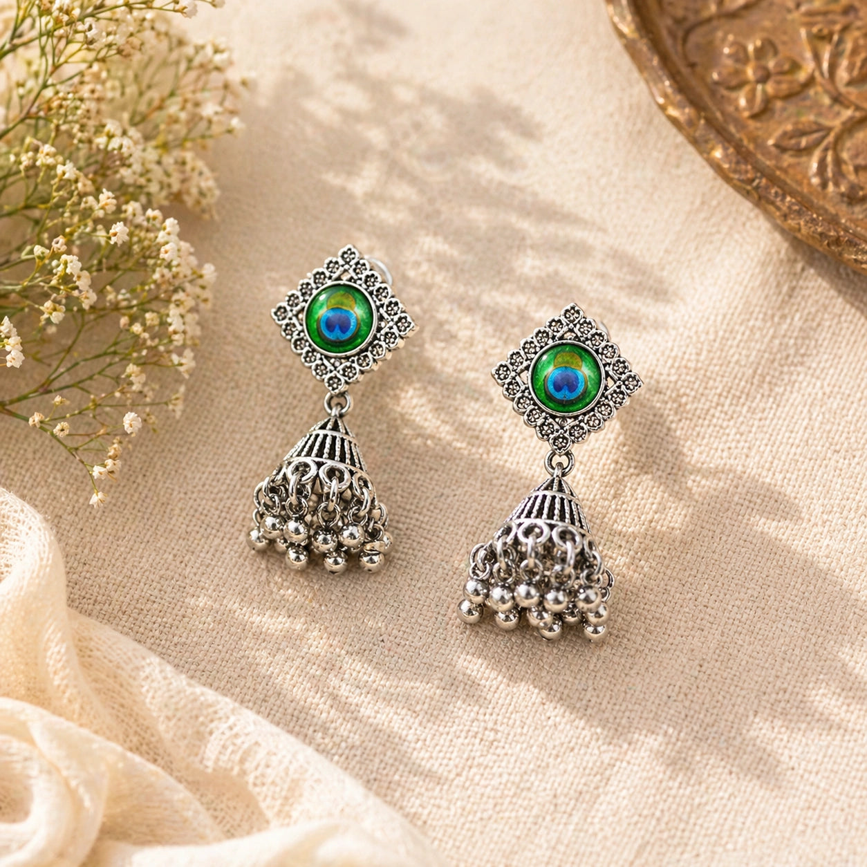Pair of silver earrings with green gemstones on a beige fabric background