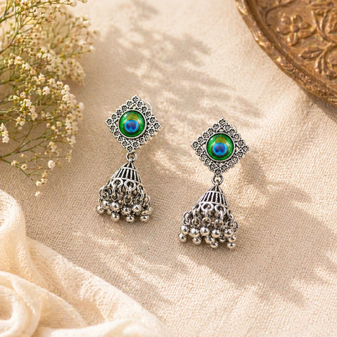Pair of silver earrings with green gemstones on a beige fabric background