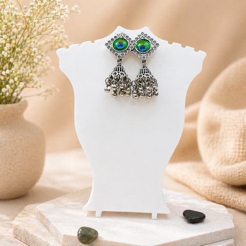 Pair of earrings with green gemstones on a white stand with a natural background