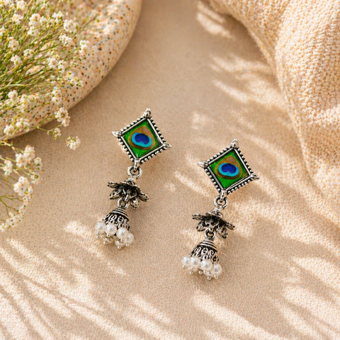 Pair of earrings with peacock feather design on a beige fabric background