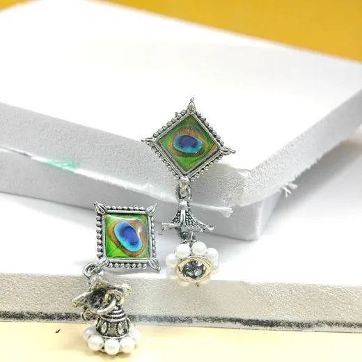 Pair of earrings with peacock feather design on a white and yellow background