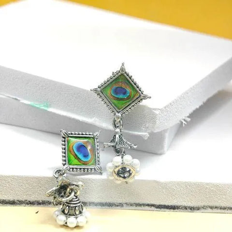 Pair of earrings with peacock feather design on a white and yellow background