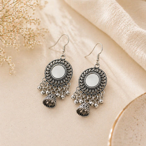 Pair of silver earrings with circular designs and dangling elements on a beige fabric background.