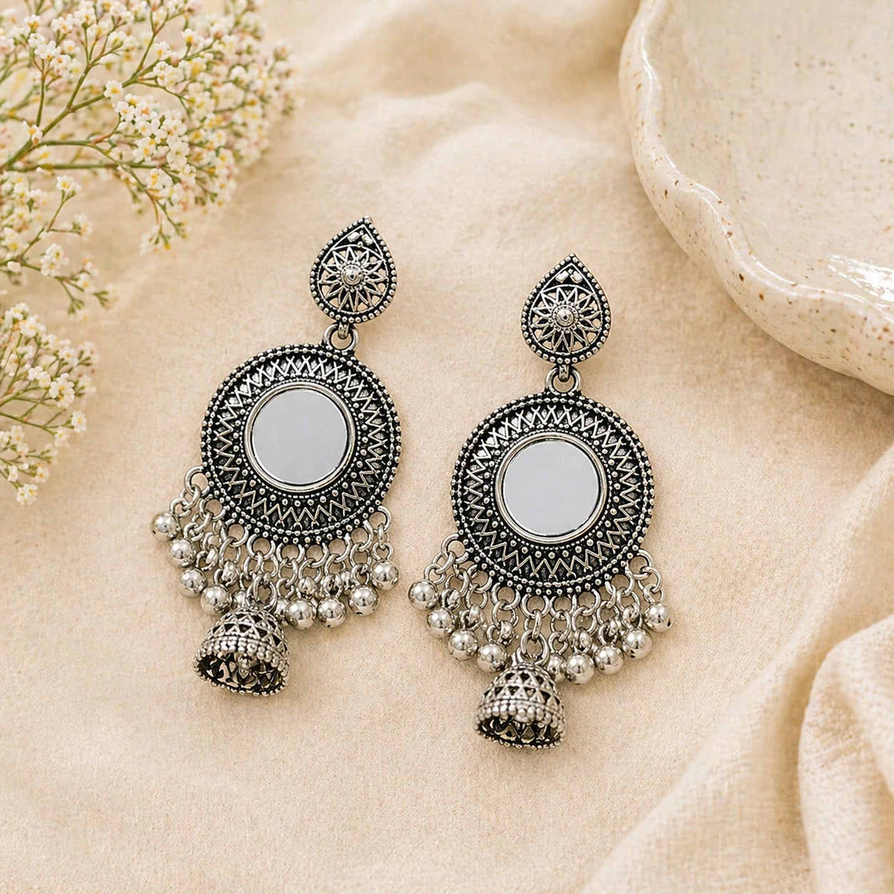 Pair of silver earrings with intricate designs on a beige fabric background