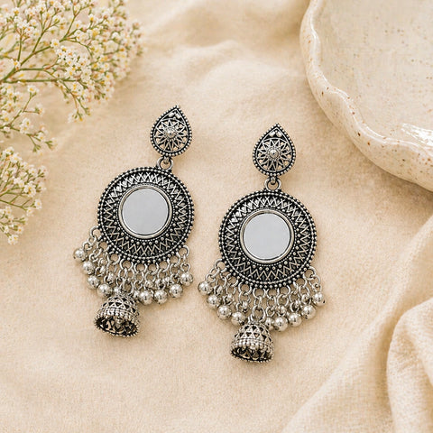 Pair of silver earrings with intricate designs on a beige fabric background