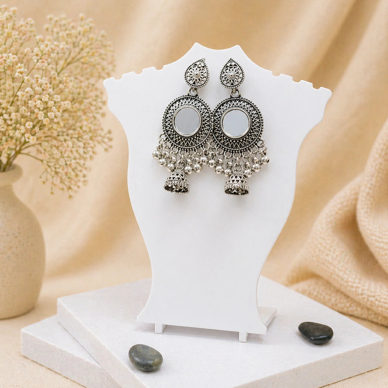 Pair of silver earrings on a white stand with a soft beige background