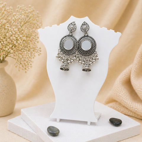 Pair of silver earrings on a white stand with a soft beige background