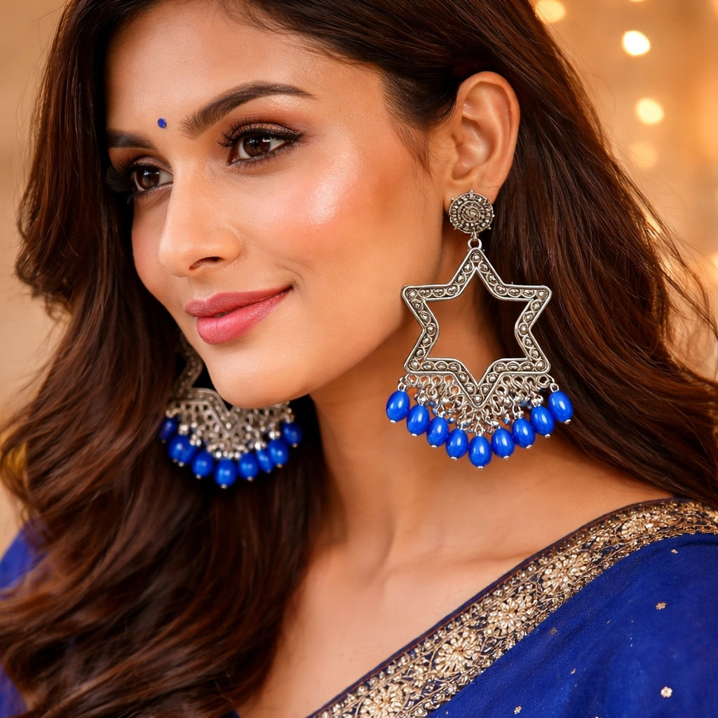 Woman wearing large star-shaped earrings with blue beads against a warm-toned background