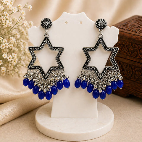 Star-shaped earrings with blue beads on a white stand with a neutral background