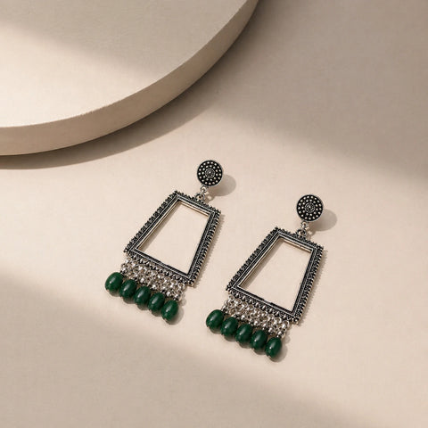 oxidised silver trapezium mirror drop earrings with green beads placed on beige surface top view jewellery image