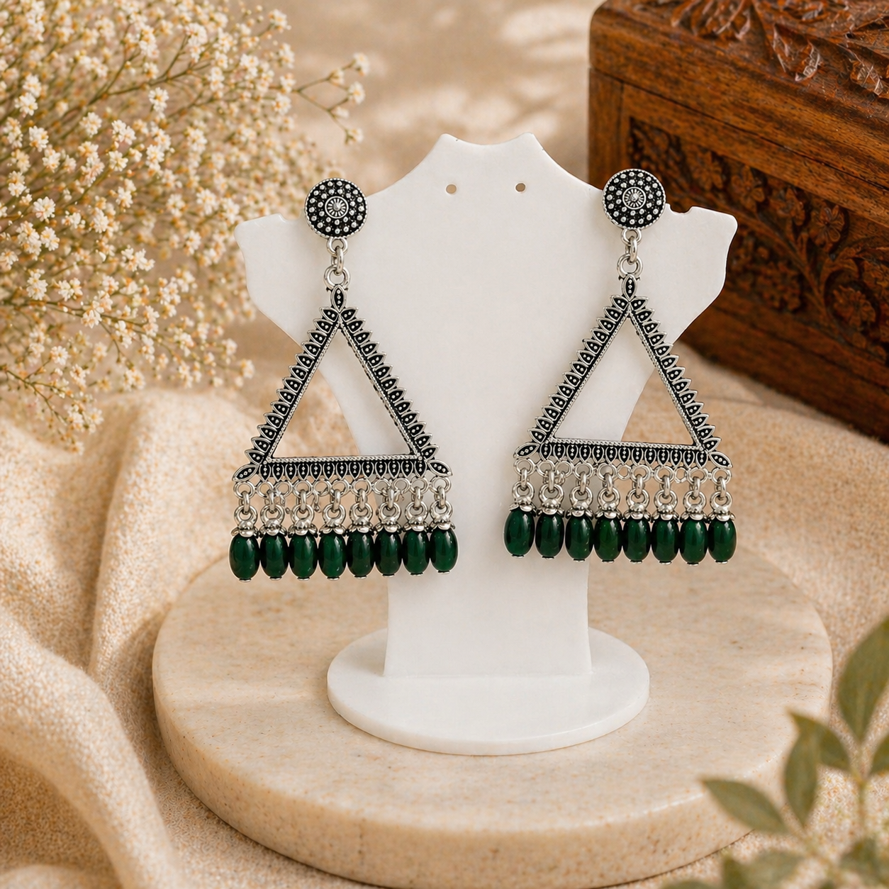 Pair of green and silver earrings on a white stand with a beige background