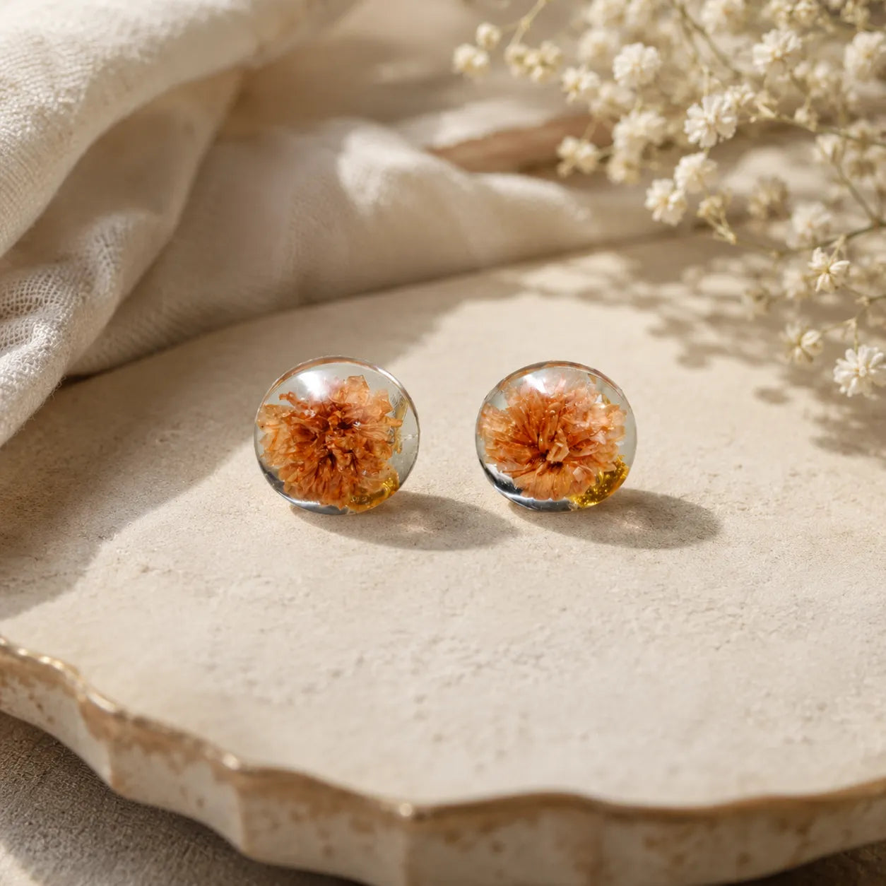 Handmade peach floral resin stud earrings with dried flower detailing and glossy transparent dome finish displayed on an aesthetic ceramic tray.