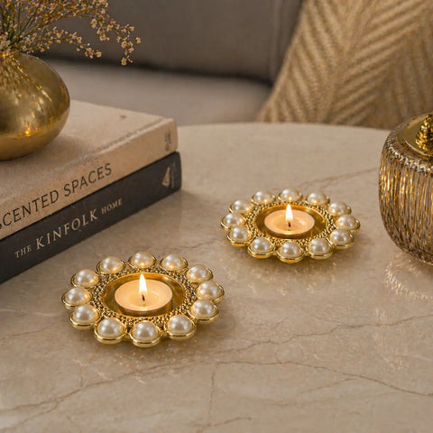 Decorative candles in pearl holders on a marble surface with books and a vase in the background.