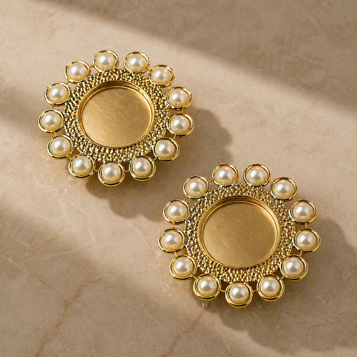 Pair of gold earrings with pearl accents on a beige marble surface