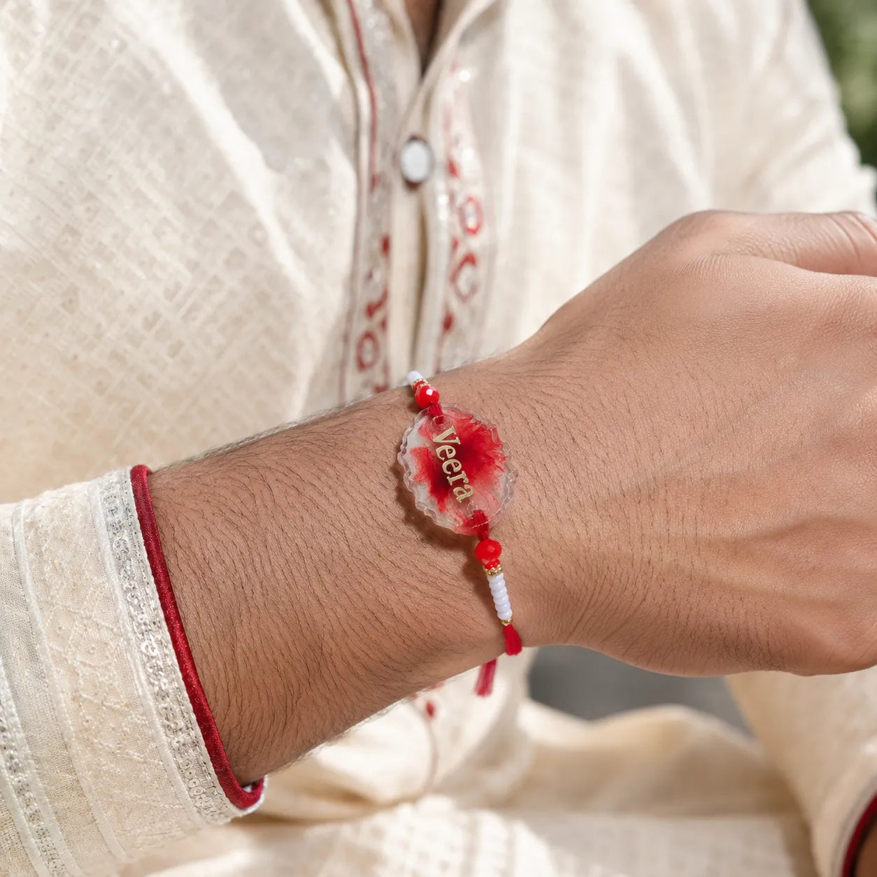 Person wearing a red bracelet with a heart-shaped charm on a blurred background