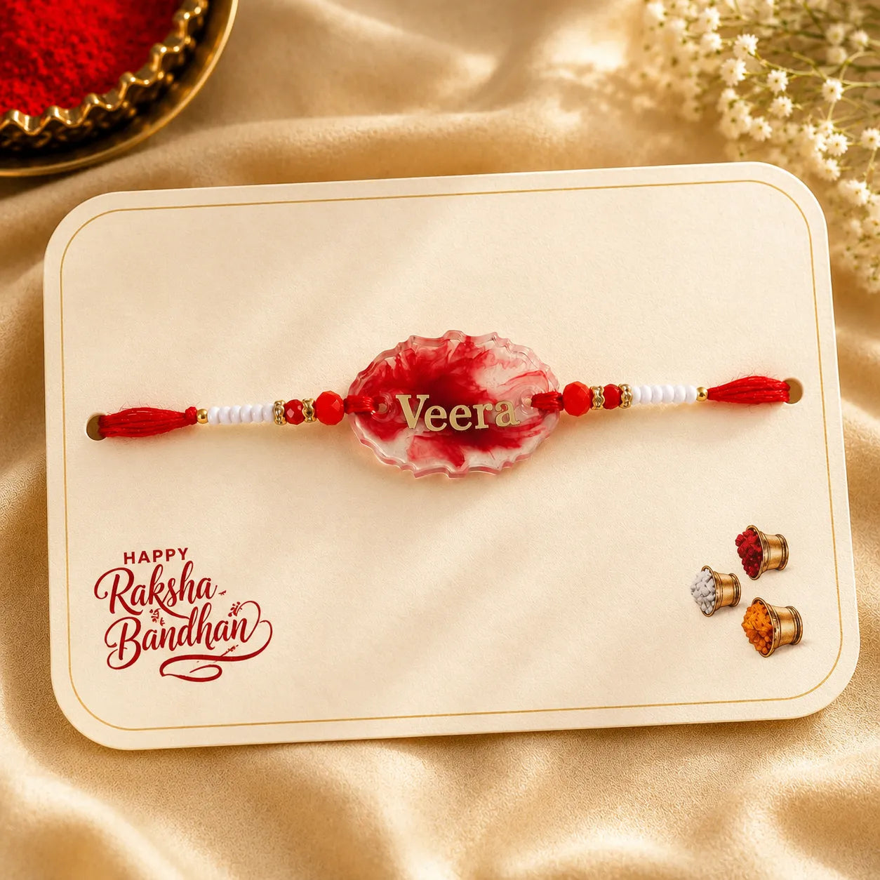 Decorative red and white Rakhi on a card with 'Happy Raksha Bandhan' text, placed on a beige fabric background.