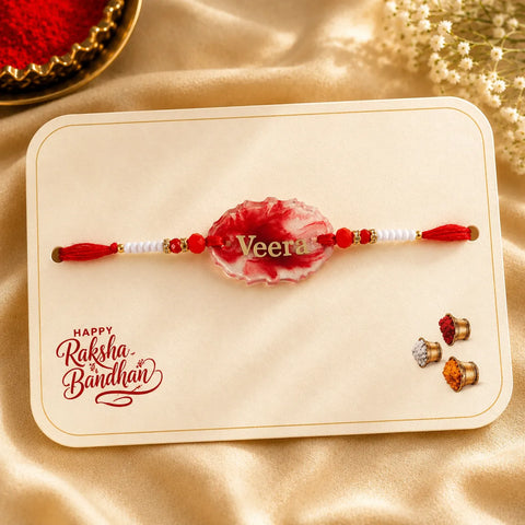 Decorative red and white Rakhi on a card with 'Happy Raksha Bandhan' text, placed on a beige fabric background.