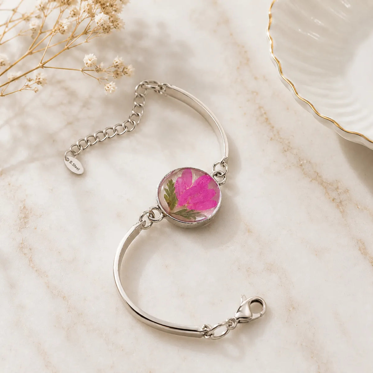 Silver bracelet with a pink floral charm on a marble surface