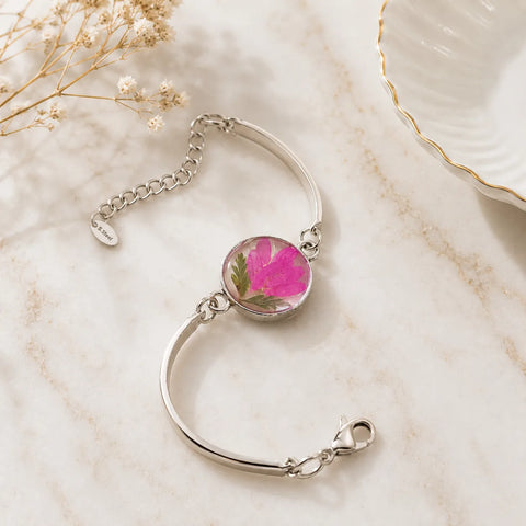 Silver bracelet with a pink floral charm on a marble surface
