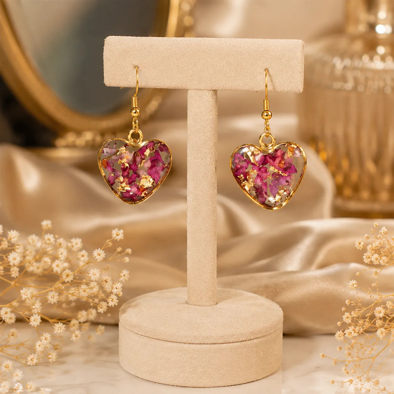 Pink floral heart resin drop earrings with gold flakes hanging on a premium beige jewellery stand with elegant luxury background and glossy handmade finish