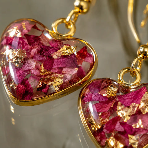 Extreme close-up of pink floral heart resin earrings with glossy transparent finish, real dried flower petals, gold flakes detailing, and elegant gold border craftsmanship
