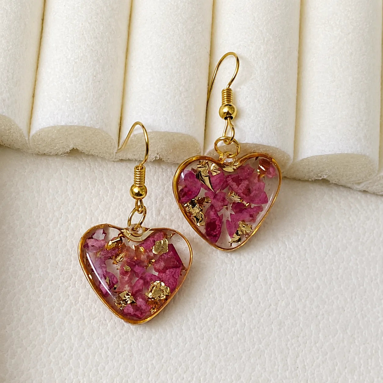 Pink floral heart resin drop earrings with gold flakes and gold border displayed on a soft cream jewellery stand with glossy handmade finish