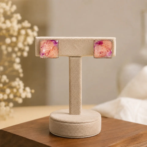 Pair of square earrings with floral design on a beige stand against a blurred indoor background