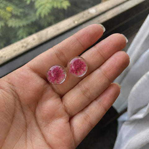Handmade pink floral resin stud earrings with real dried flower detailing held in hand near natural daylight window lighting.