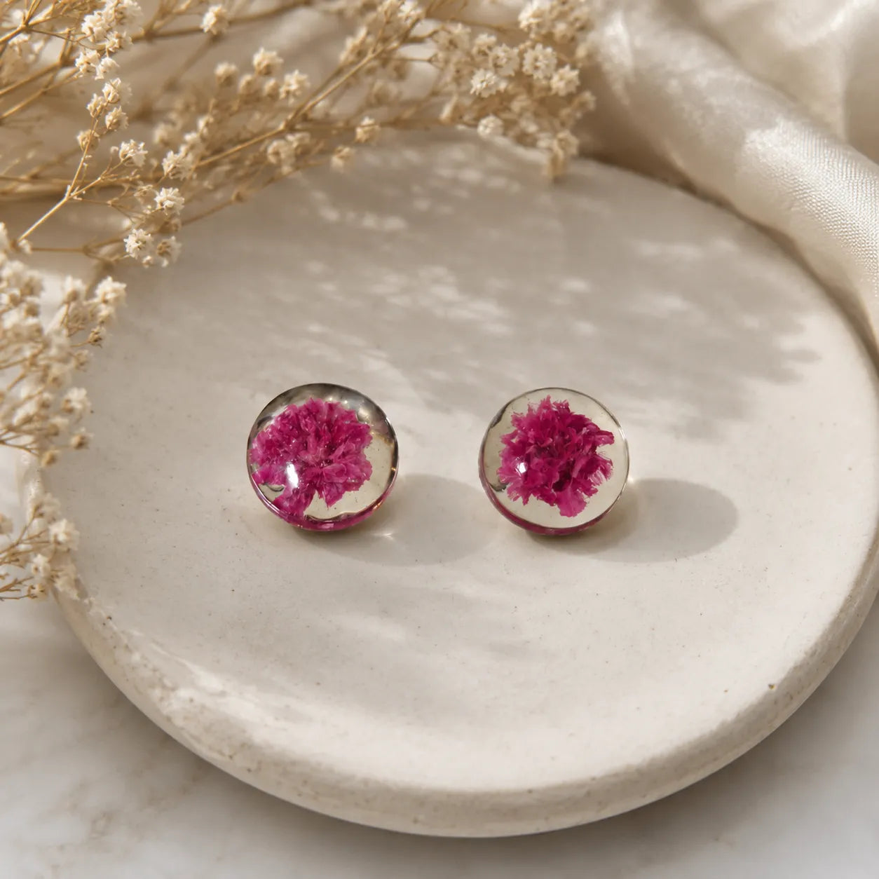 Handmade pink floral resin stud earrings with real dried flower detailing displayed on a ceramic tray with soft luxury aesthetic styling.