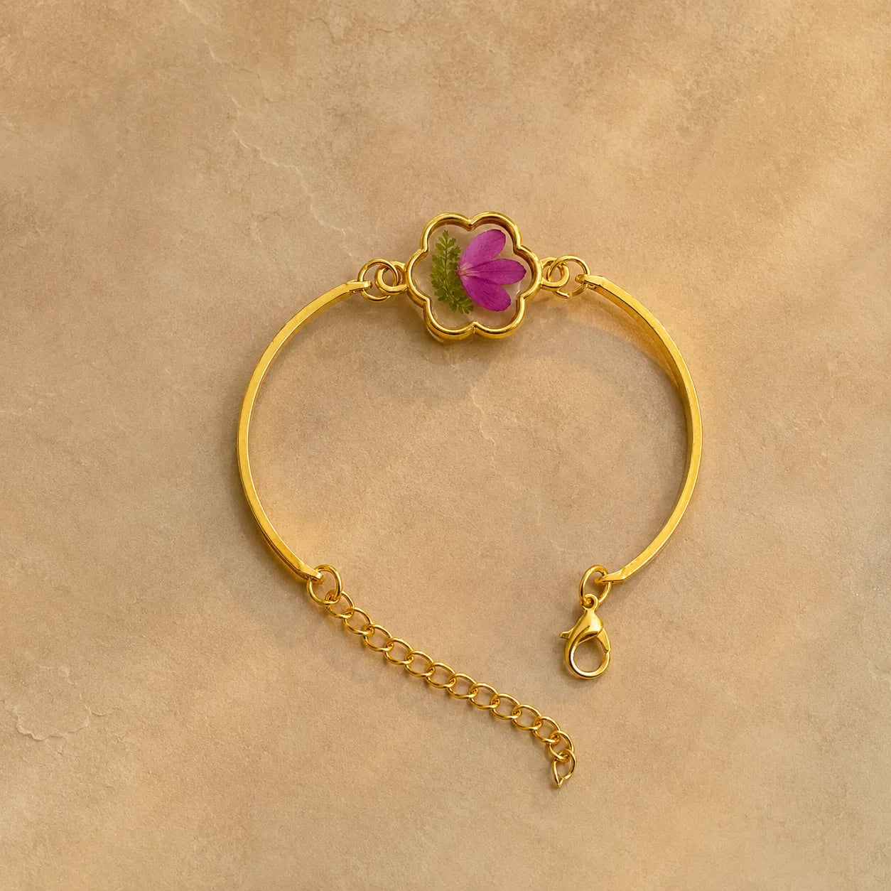 Gold bracelet with a pink flower charm on a beige background